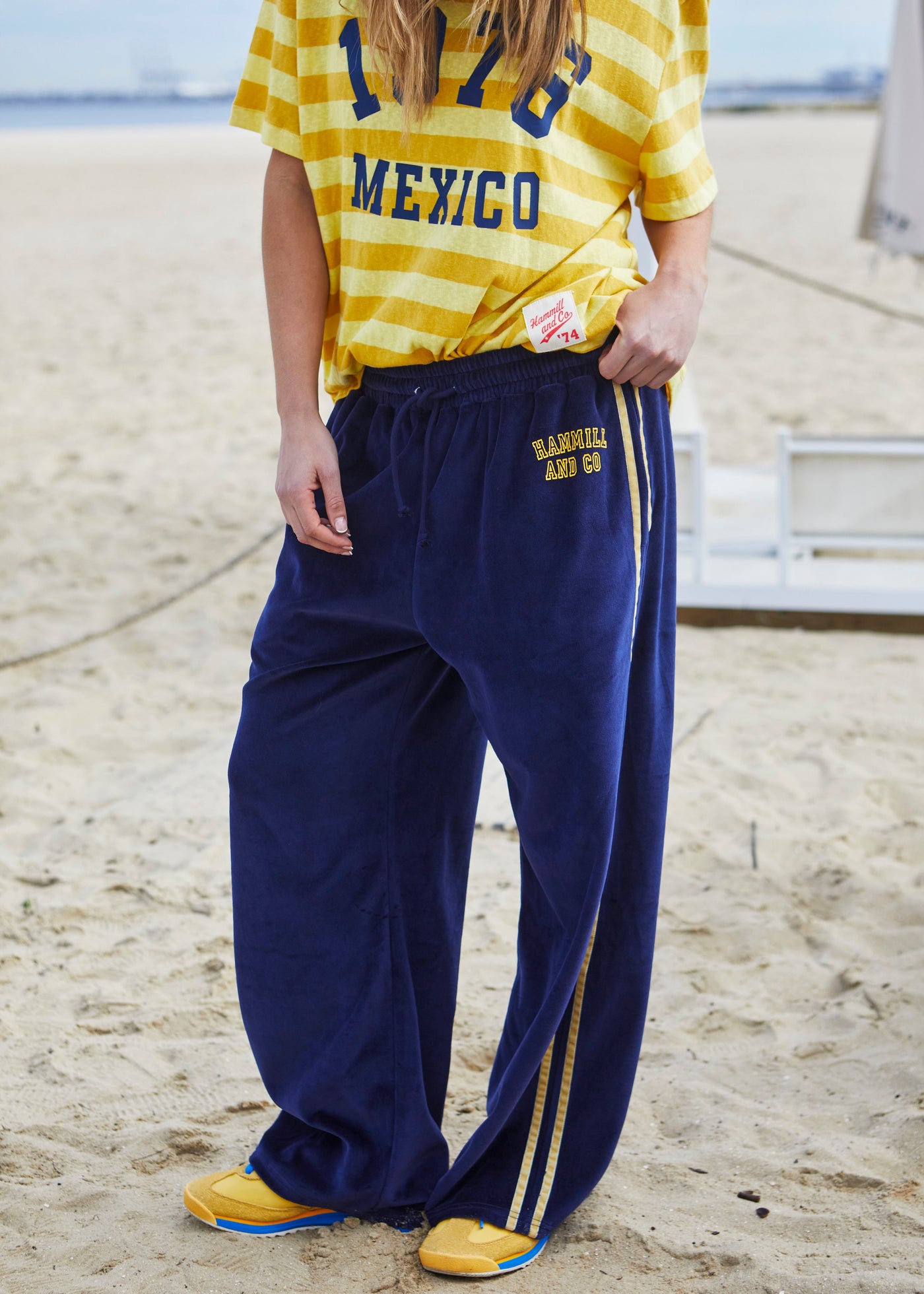 Hammill & Co New wider leg track pant in our luxurious, lightweight velour with velour stripes down each leg, draw cord and Hammill and Co logo print on left hem. The fit is a true to size, not oversized.