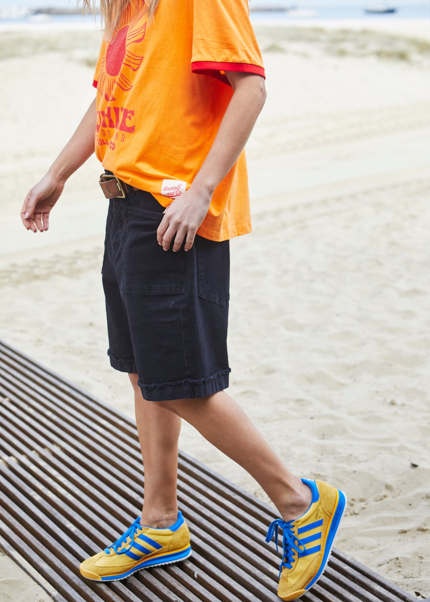 Hammill & Co pair of longer-length black stretch denim shorts with a relaxed fit. They have front pockets, a raw rolled hem, and sit mid-thigh