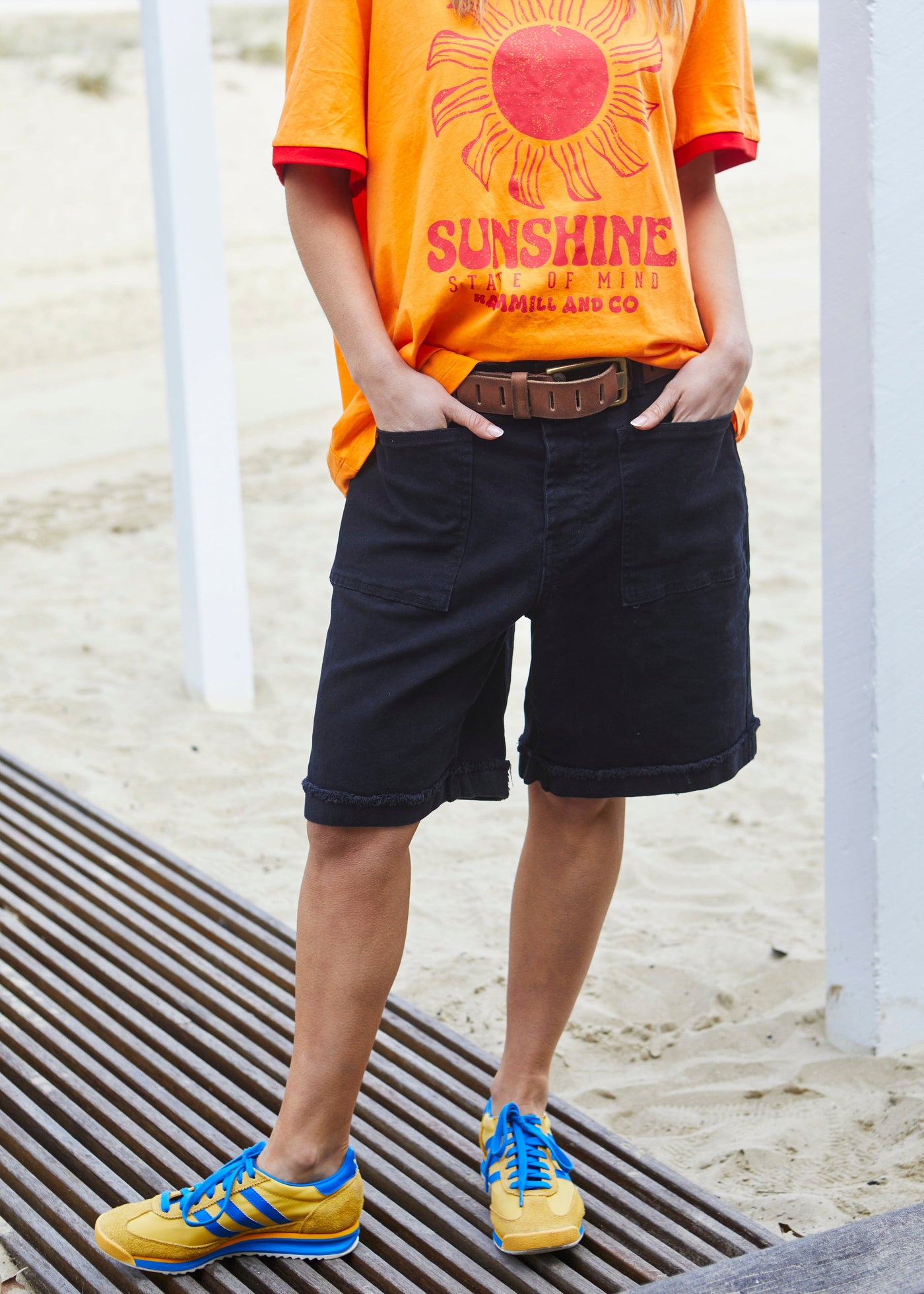 Hammill & Co pair of longer-length black stretch denim shorts with a relaxed fit. They have front pockets, a raw rolled hem, and sit mid-thigh